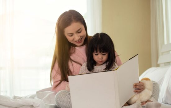 A mother reading a book with her daughter on a bed
