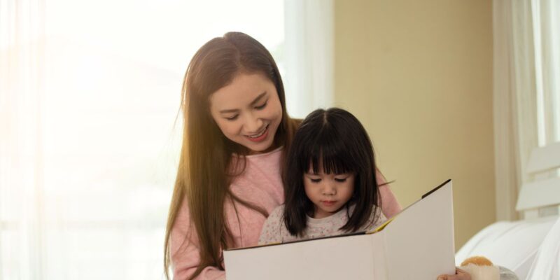 A mother reading a book with her daughter on a bed