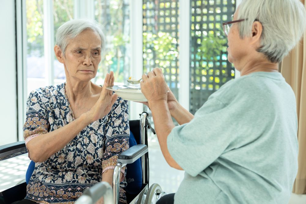 An elderly woman declining more food from another elderly woman