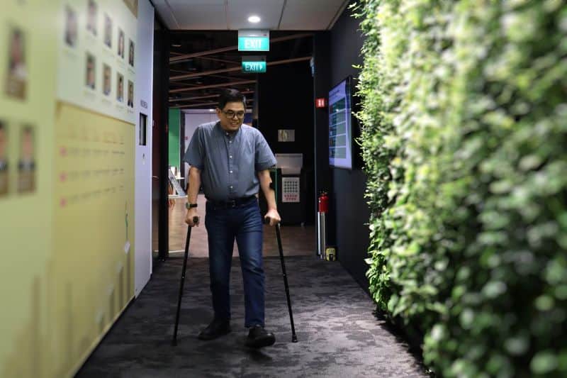 Mr CHong walking along an office corridor with the aid of his crutches.