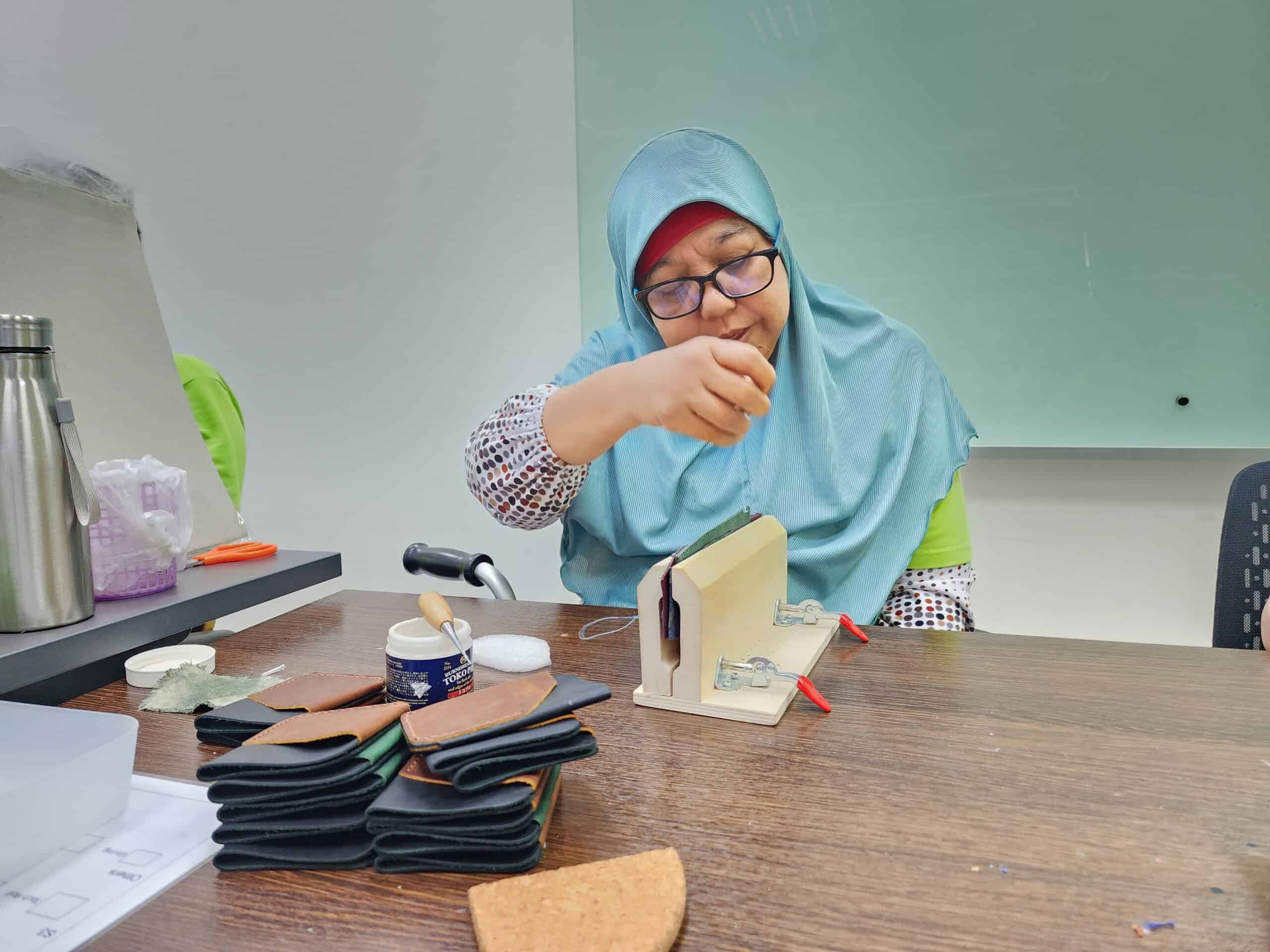 Mdm Hamidah sewing a leather piece that is held steady by a wooden clamp