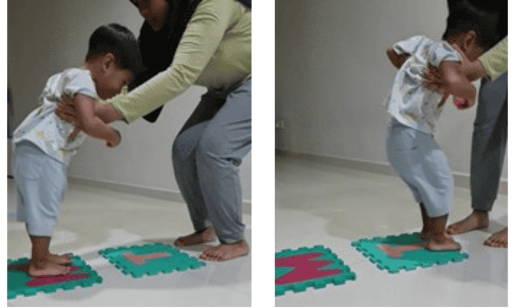 A caregiver supporting a young boy under his arms to help him jump from one target to another.