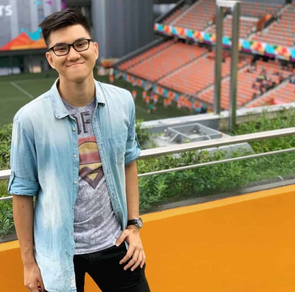 Bjorn in a blue shirt worn over a grey t-shirt, standing against a backdrop of a stadium