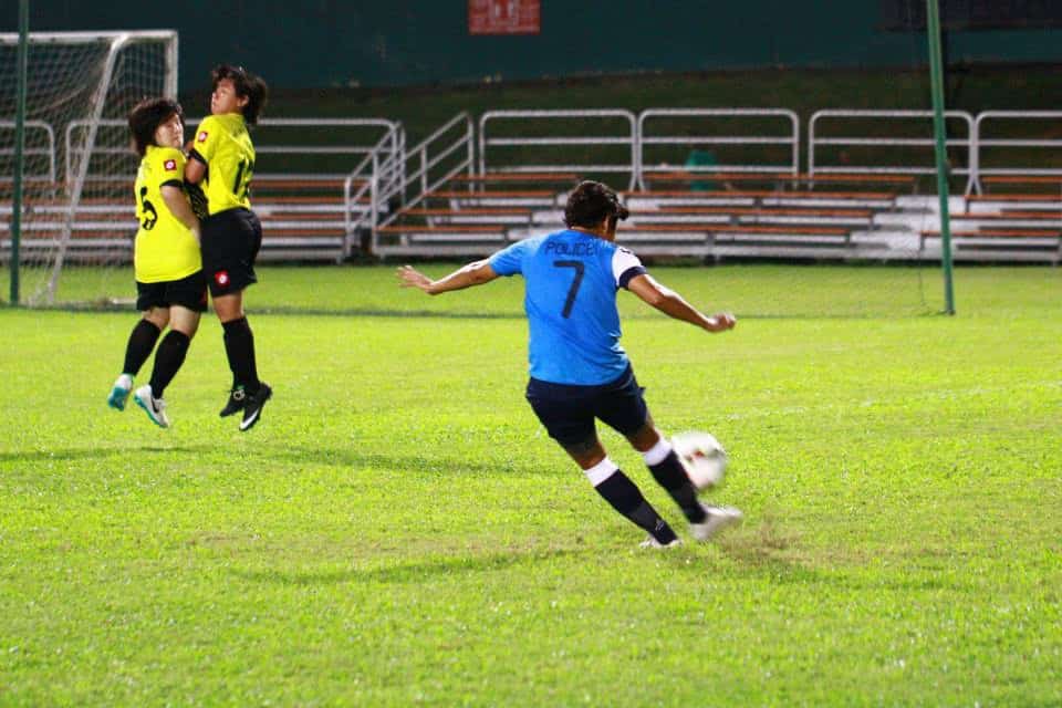 Rena and Shahidah in yellow jerseys jumping together as a wall to block a free kick from an opponent wearing blue