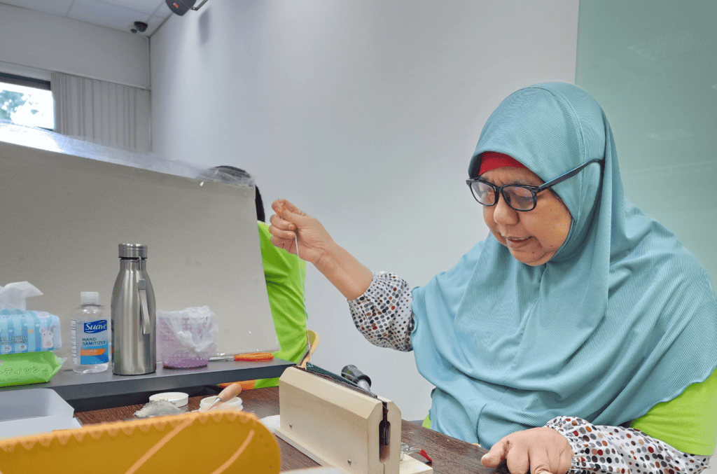 Mdm Hamidah uses a wooden clamp to secure the leather piece while she sews.