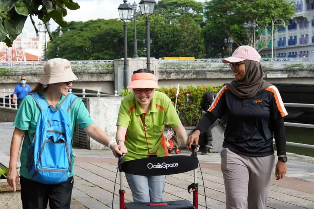 A lady using a rollator to walk, with two ladies by her side