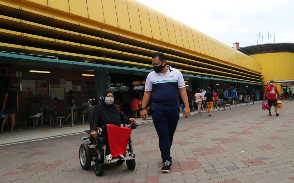 Woman on wheelchair at the hawker centre accompanied by a social worker