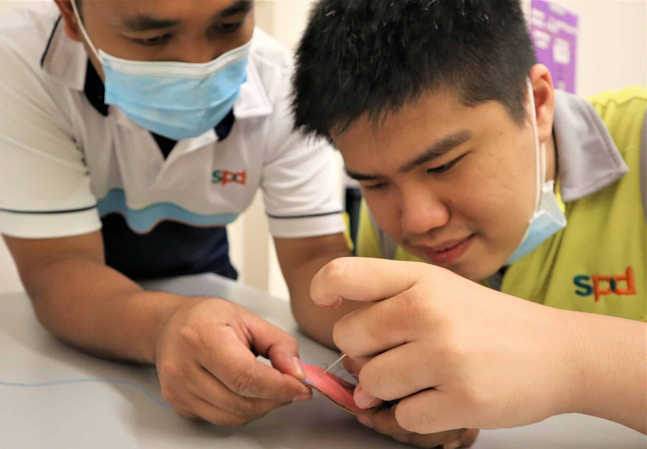 Training officer Neilson helping Hong Yun with the leathercraft activity