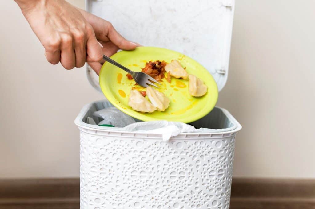 A person discarding food from a plate into a bin