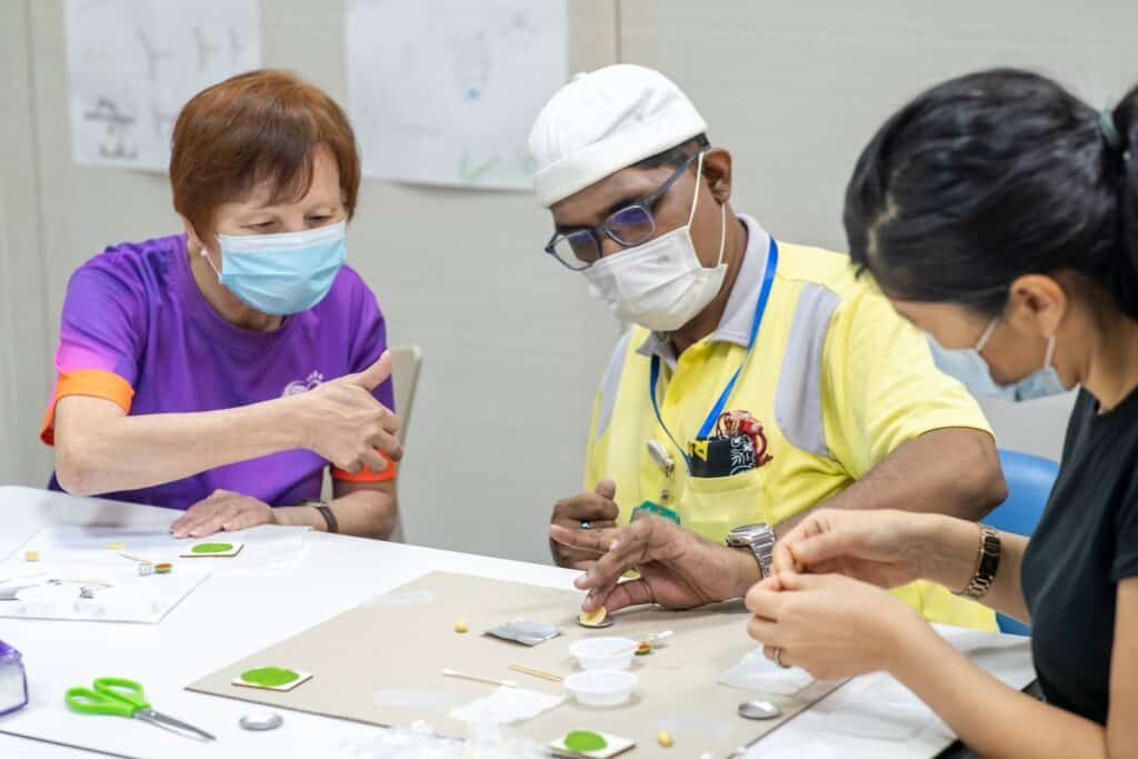 An elderly volunteer helping a day activity centre client with some art and craft