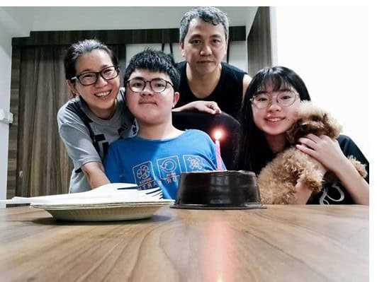 Aaron posing with his parents, sister and dog. A dark brown cake with a single lighted candle is in the foreground