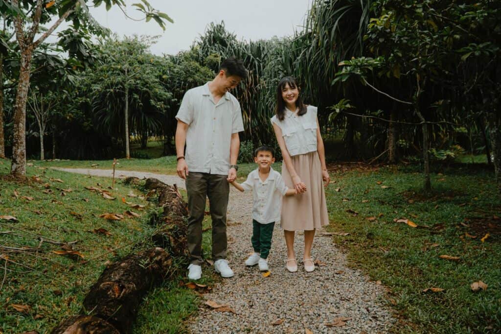 Wei Shi with her husband and Elliot strolling on a gravel path in a park