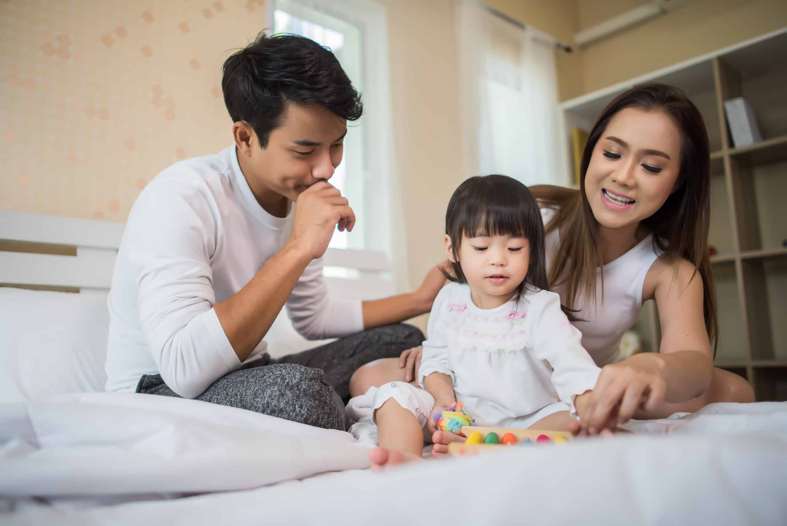 Happy child with parents playing in the bed at home