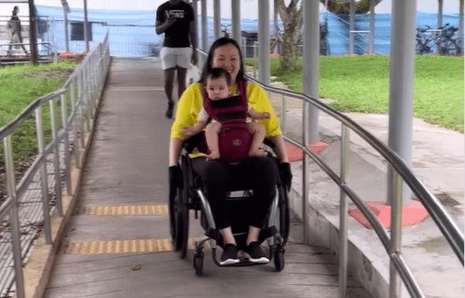 Jean using a carrier to carry Evan as she goes down the slope on her wheelchair