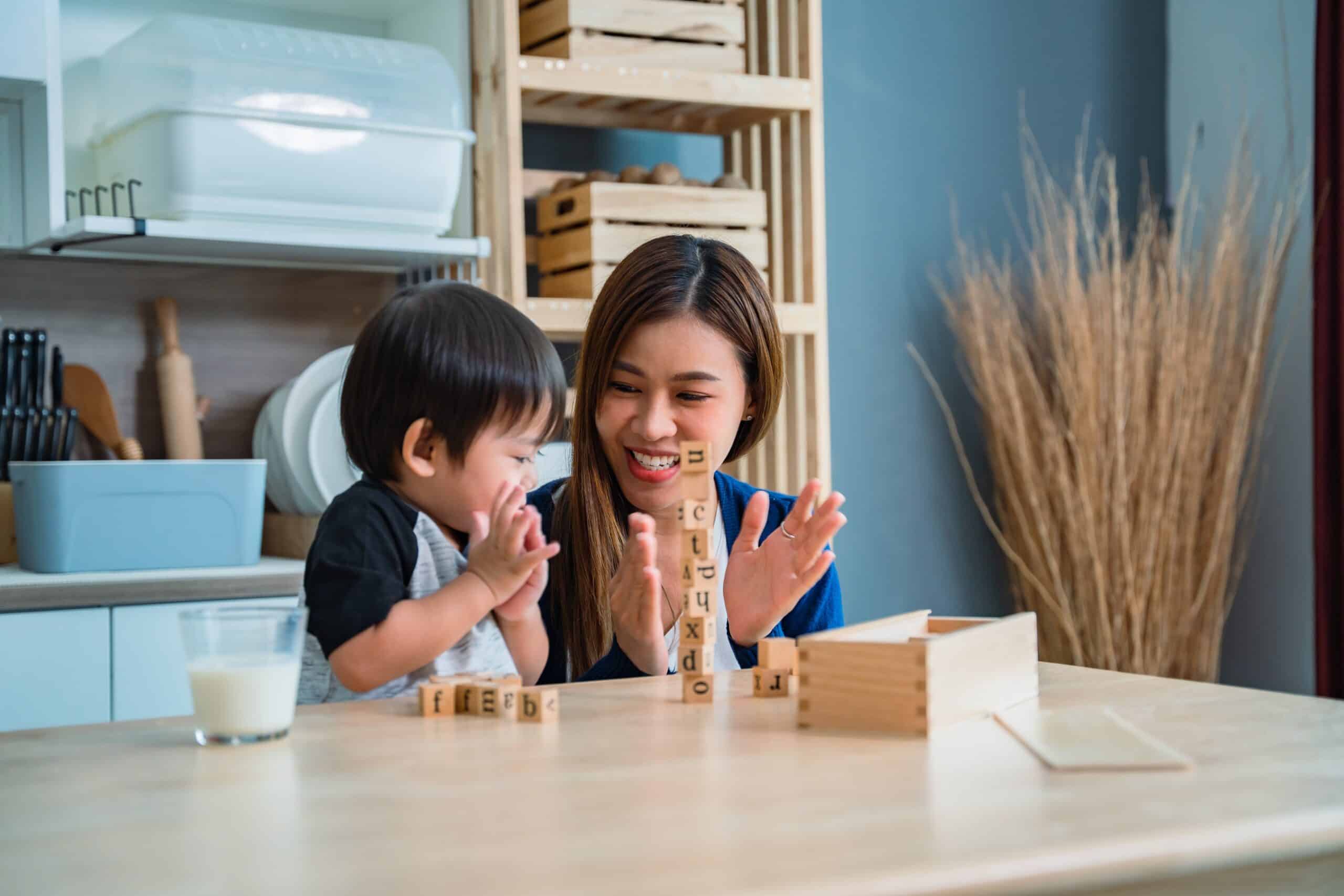 A mother clapping together with her son with a set of alphabet building blocks