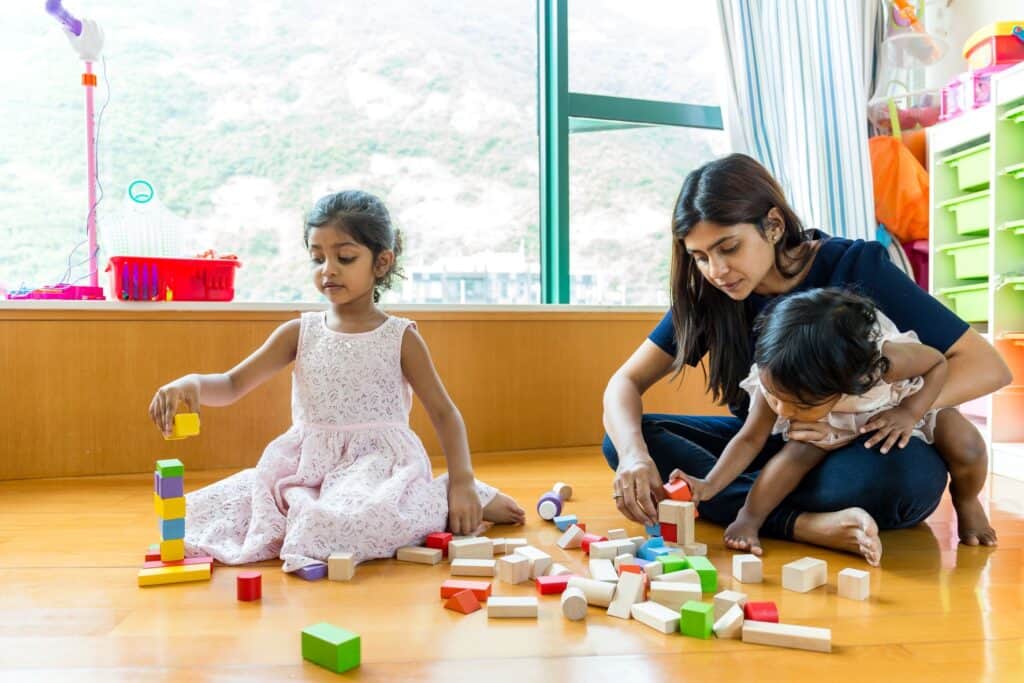 Two young girls playing blocks with their mother