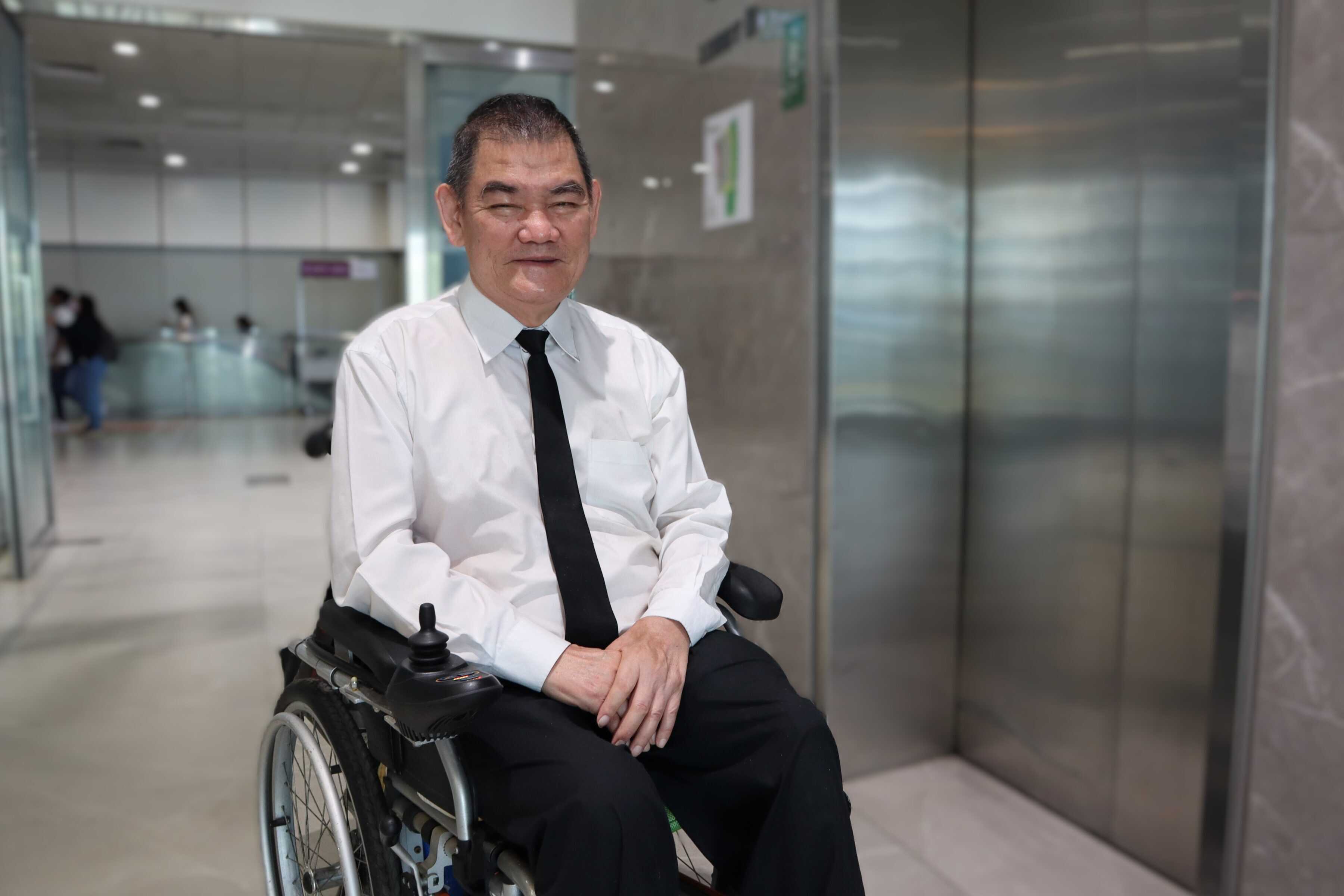 A senior wheelchair user in shirt and tie at an office building lift lobby.