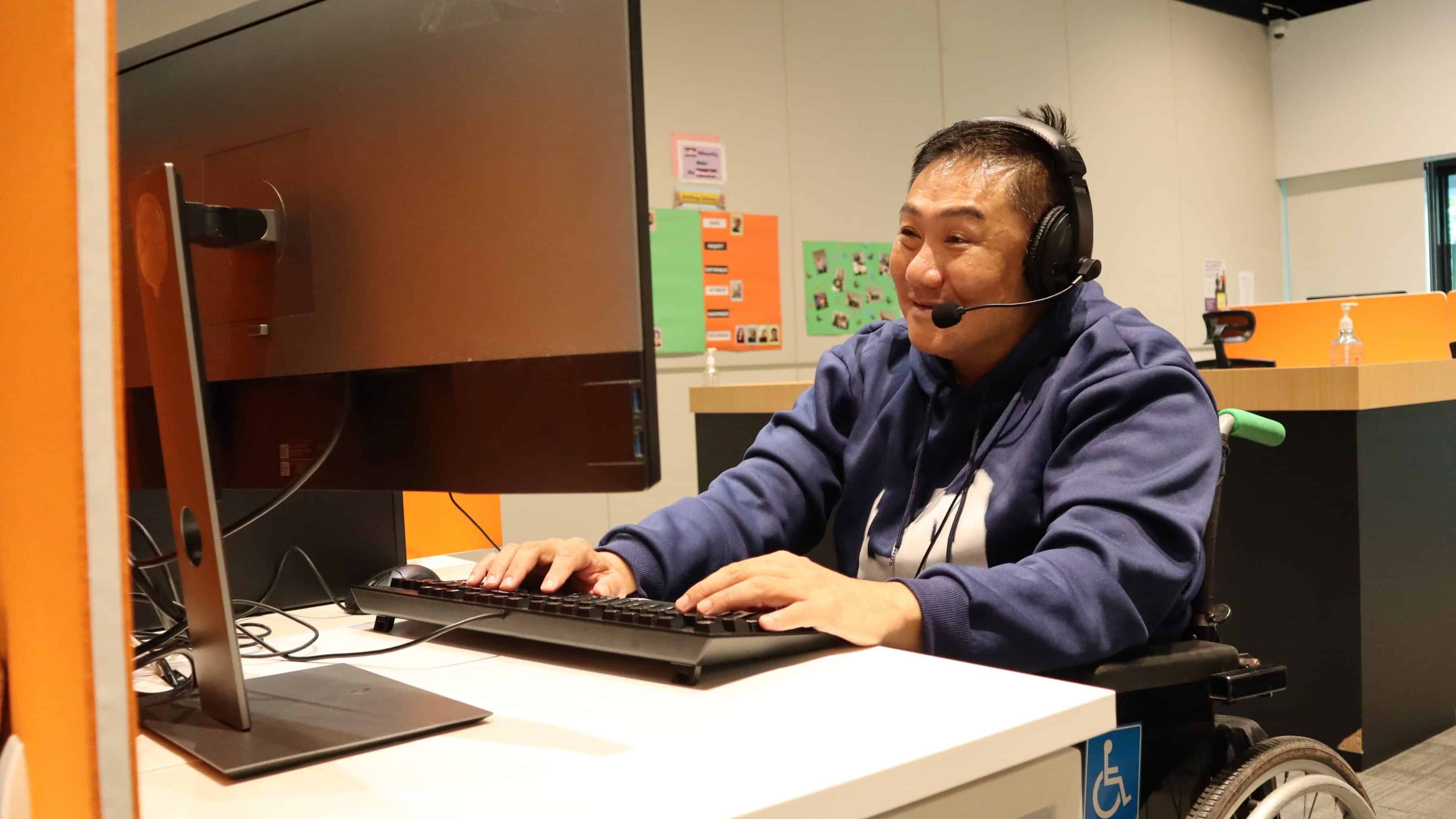 A wheelchair user wearing a headset working on his computer