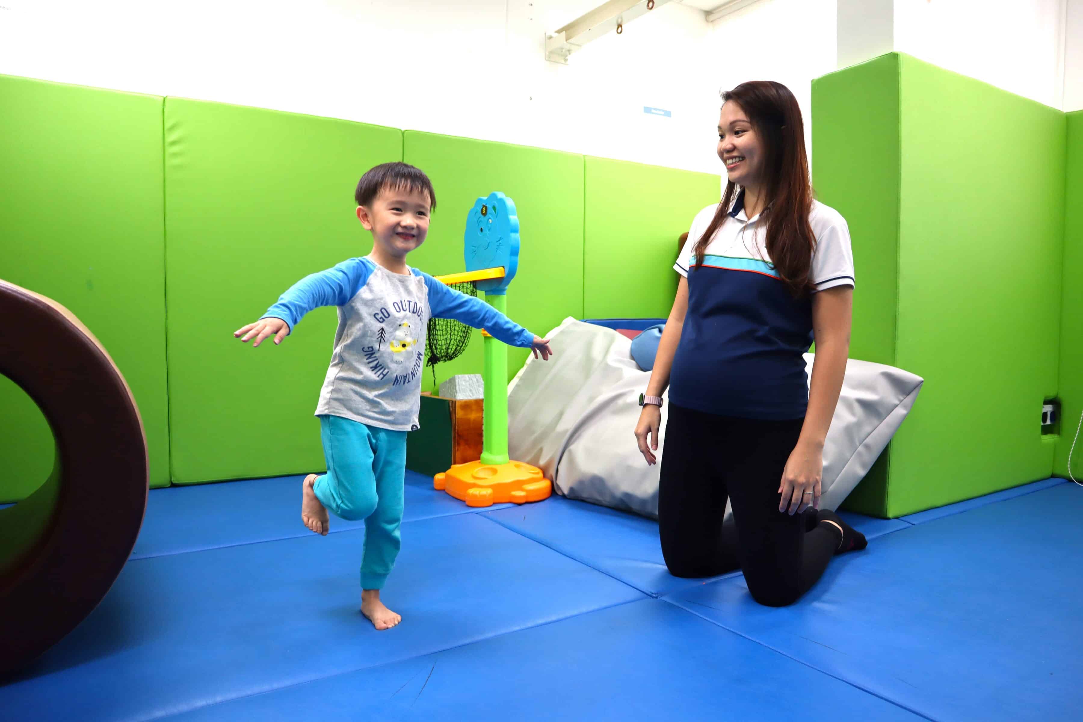 A boy balancing on one leg as an S P D therapist looks on