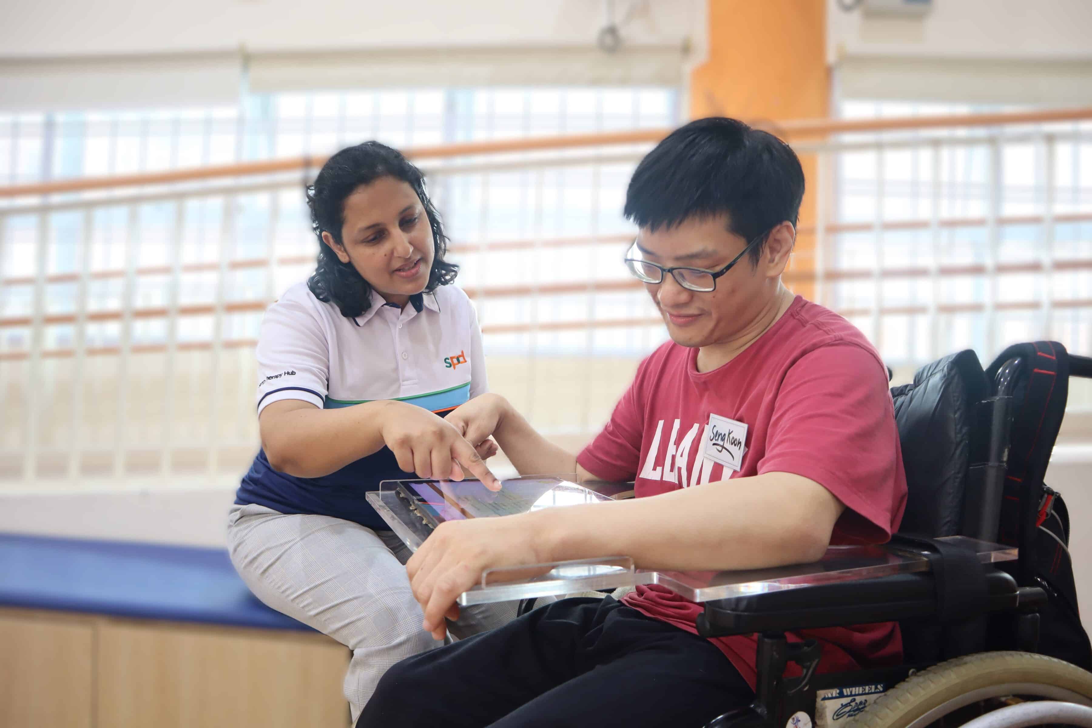 An S P D A T professional guiding a person seated in his wheelchair on using a tablet