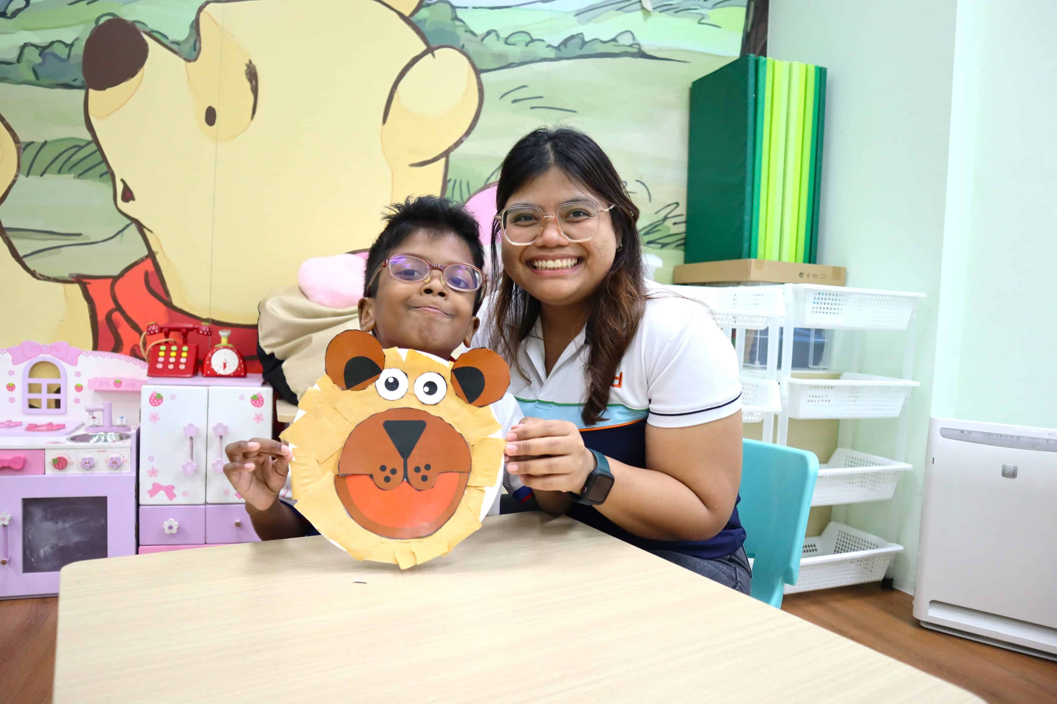 S P D early intervention teacher and a child holding up a lion-shaped craftwork