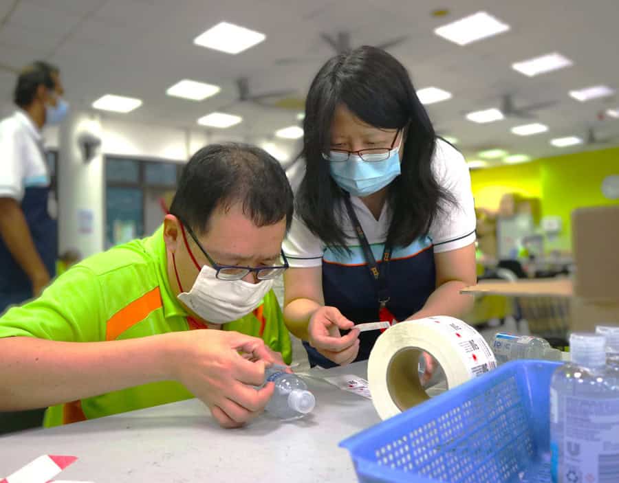 A trainee sticking labels on a bottle with guidance from an SPD workshop supervisor