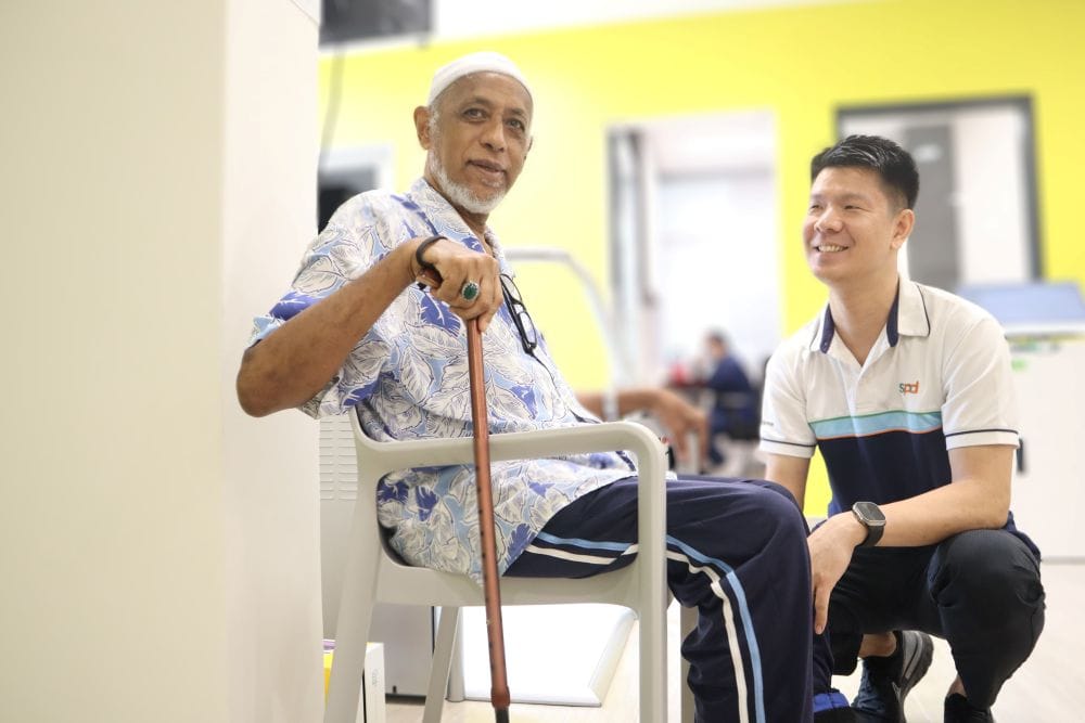 A therapist smiles and looks at an elderly man seated