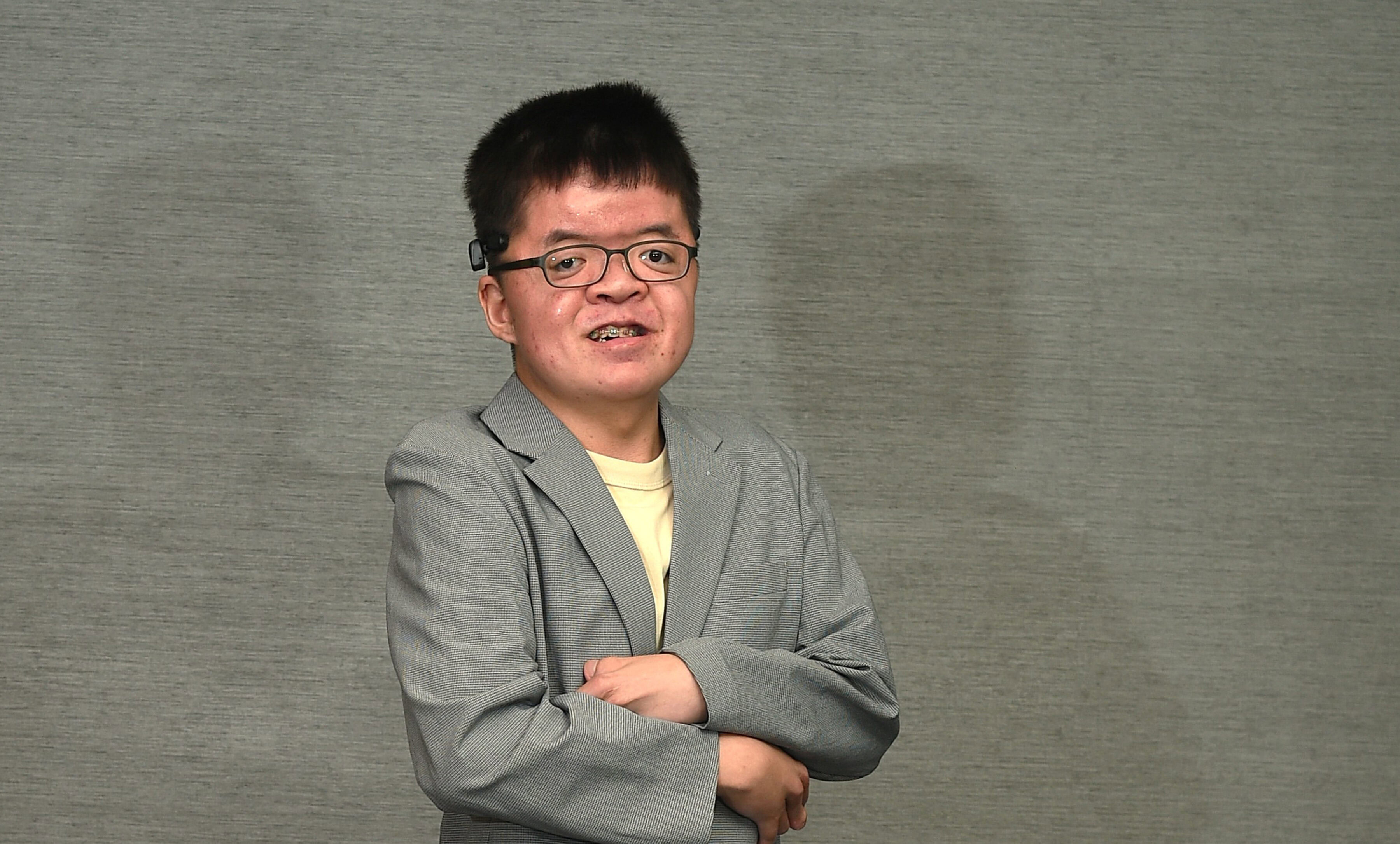 Eugene standing against a grey textured backdrop smiling with his arms folded