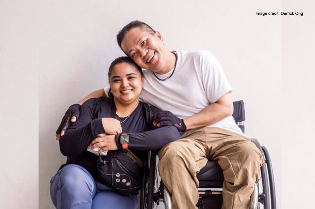 Mr Wong seated in his wheelchair with his arm around Mdm Nooraini beside him