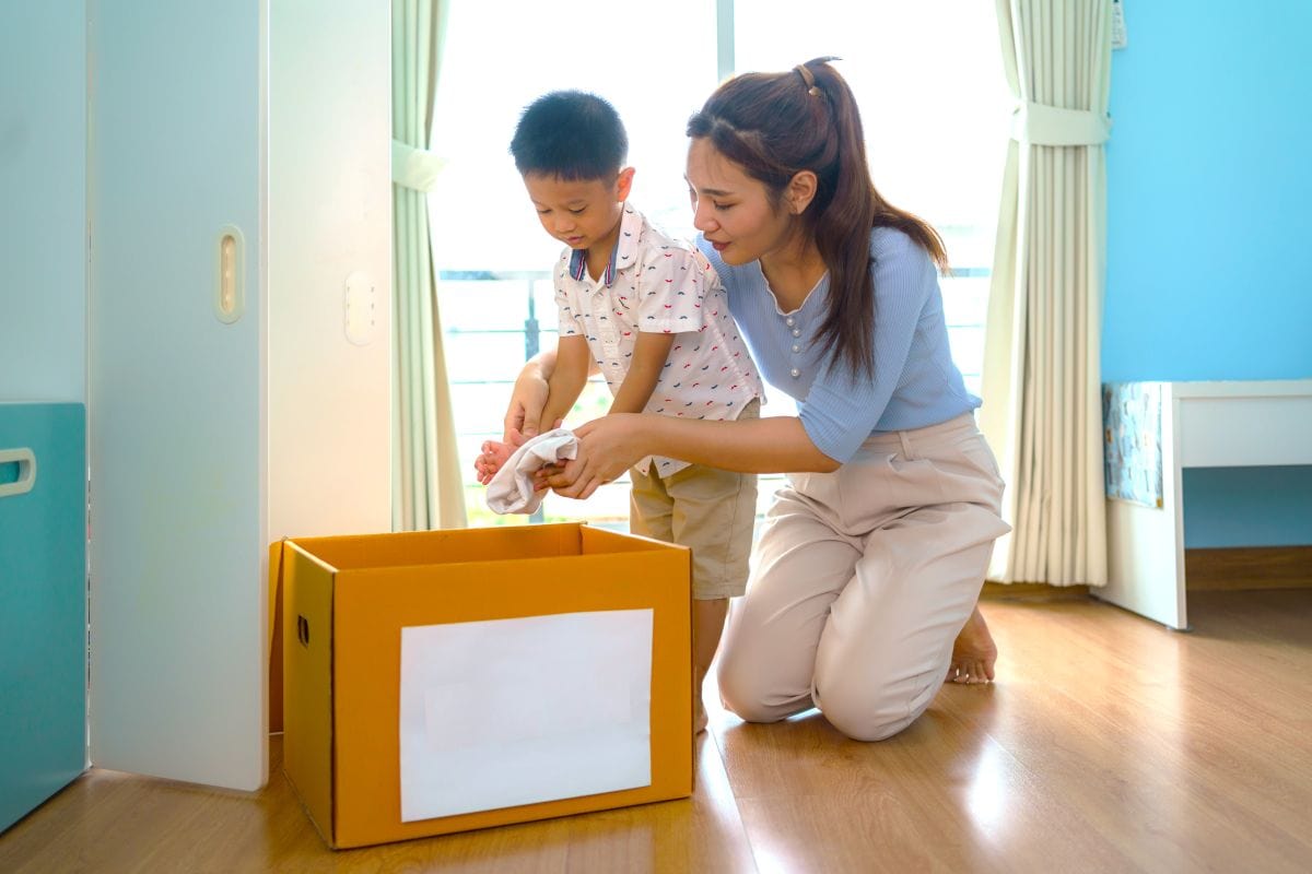 A mother guiding a boy in putting things into a box.