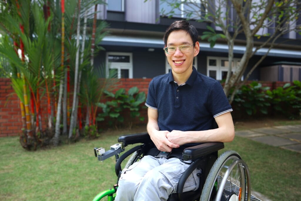 Zachary in a garden, seated in his wheelchair and smiling