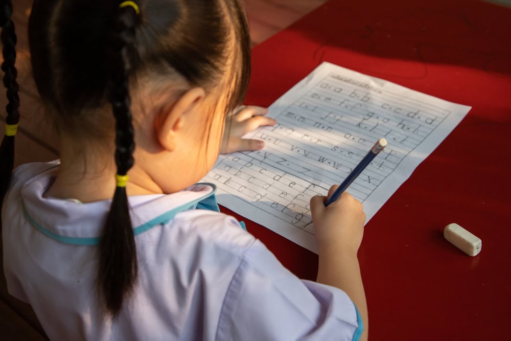 Child tracing alphabets on a worksheet.