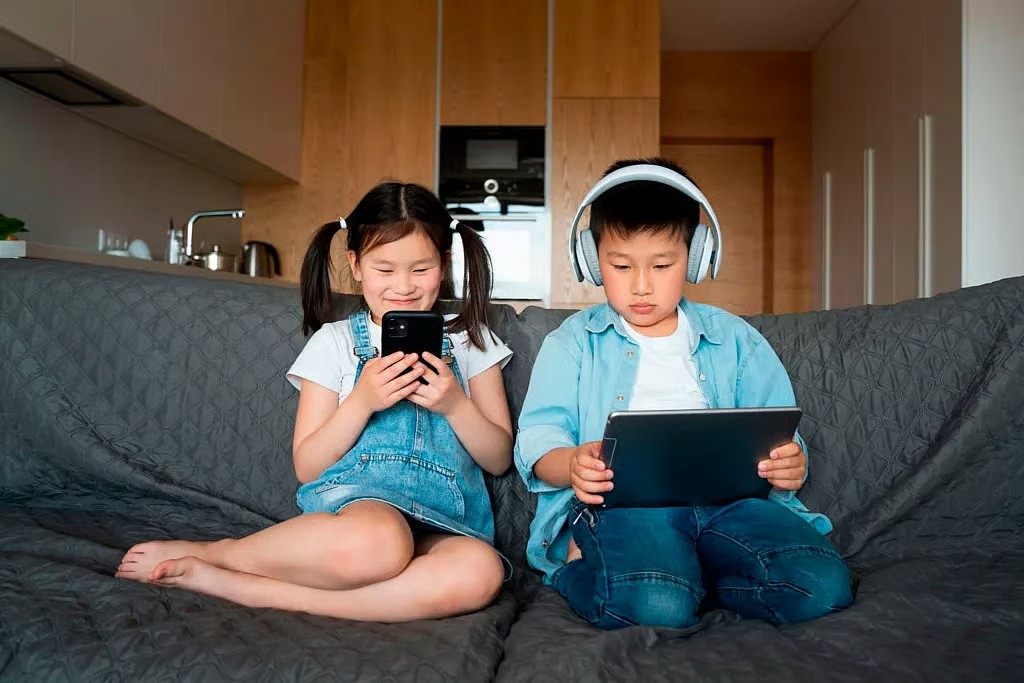 Is your child getting enough physical activity? 2 2 children seated on a sofa at home using their mobile devices.