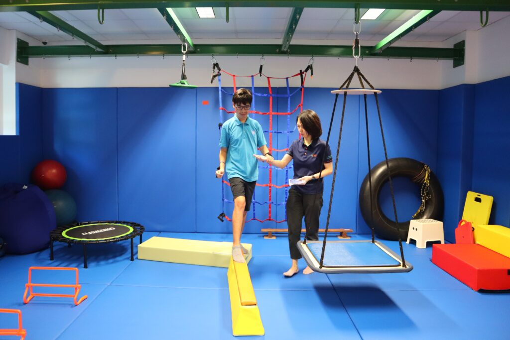Li Wen guiding a client balancing on a bean inside the occupational therapy gym